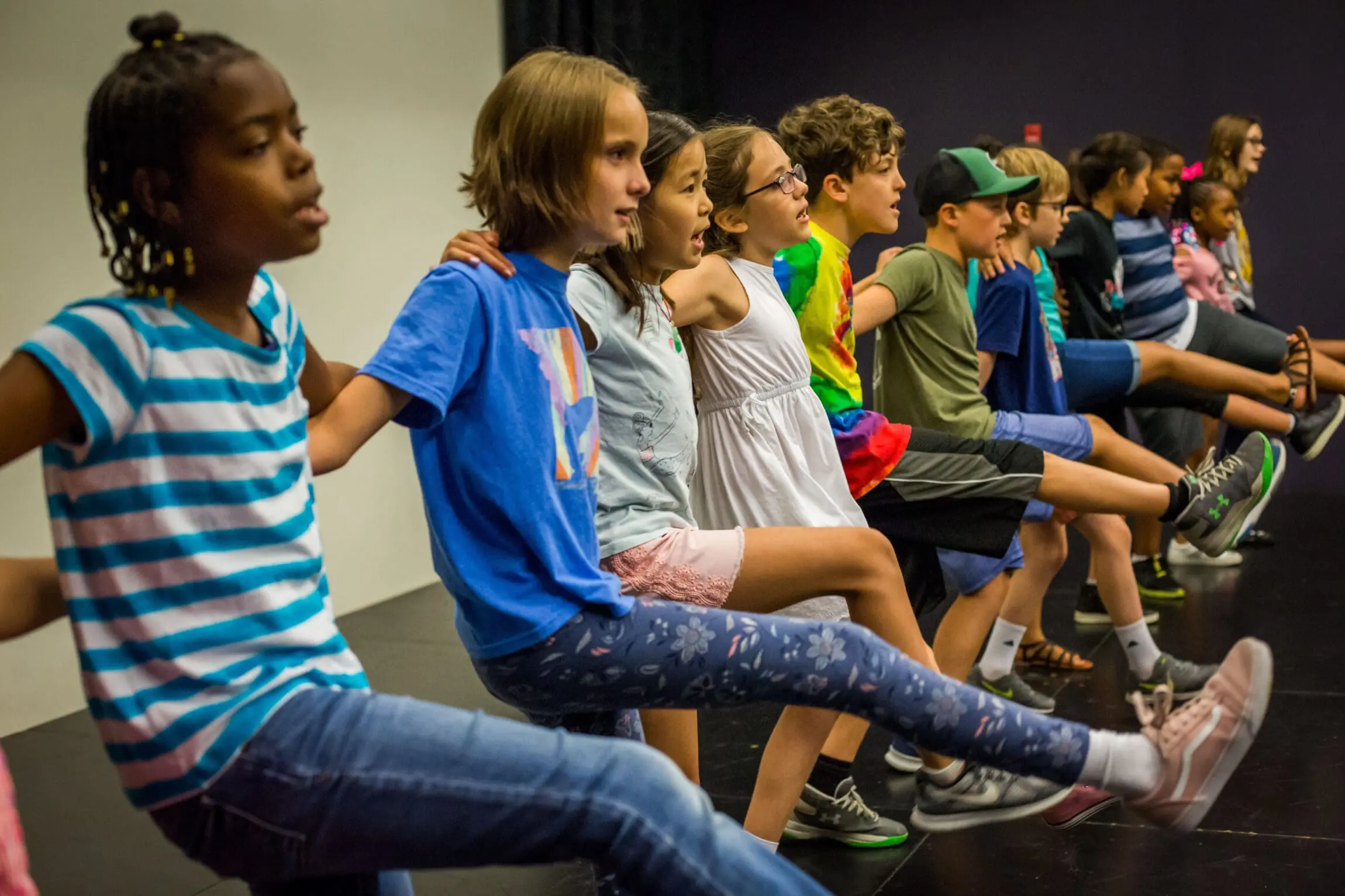 Eight kids with linked arms in a kick line.