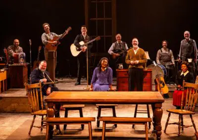 Actors holding instruments sitting behind a table.