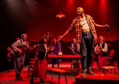 Actor standing on a chest singing while other actors are behind him singing.